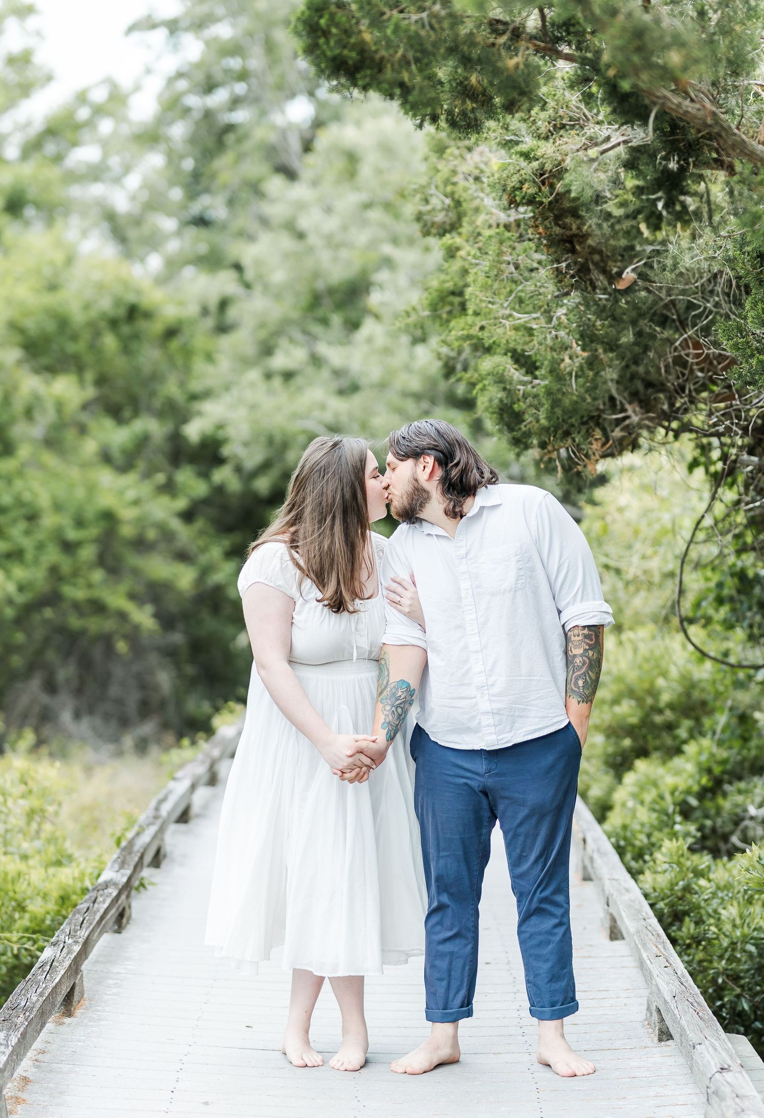 Couple shares romantic moment on wooden boardwalk surrounded by green foliage.