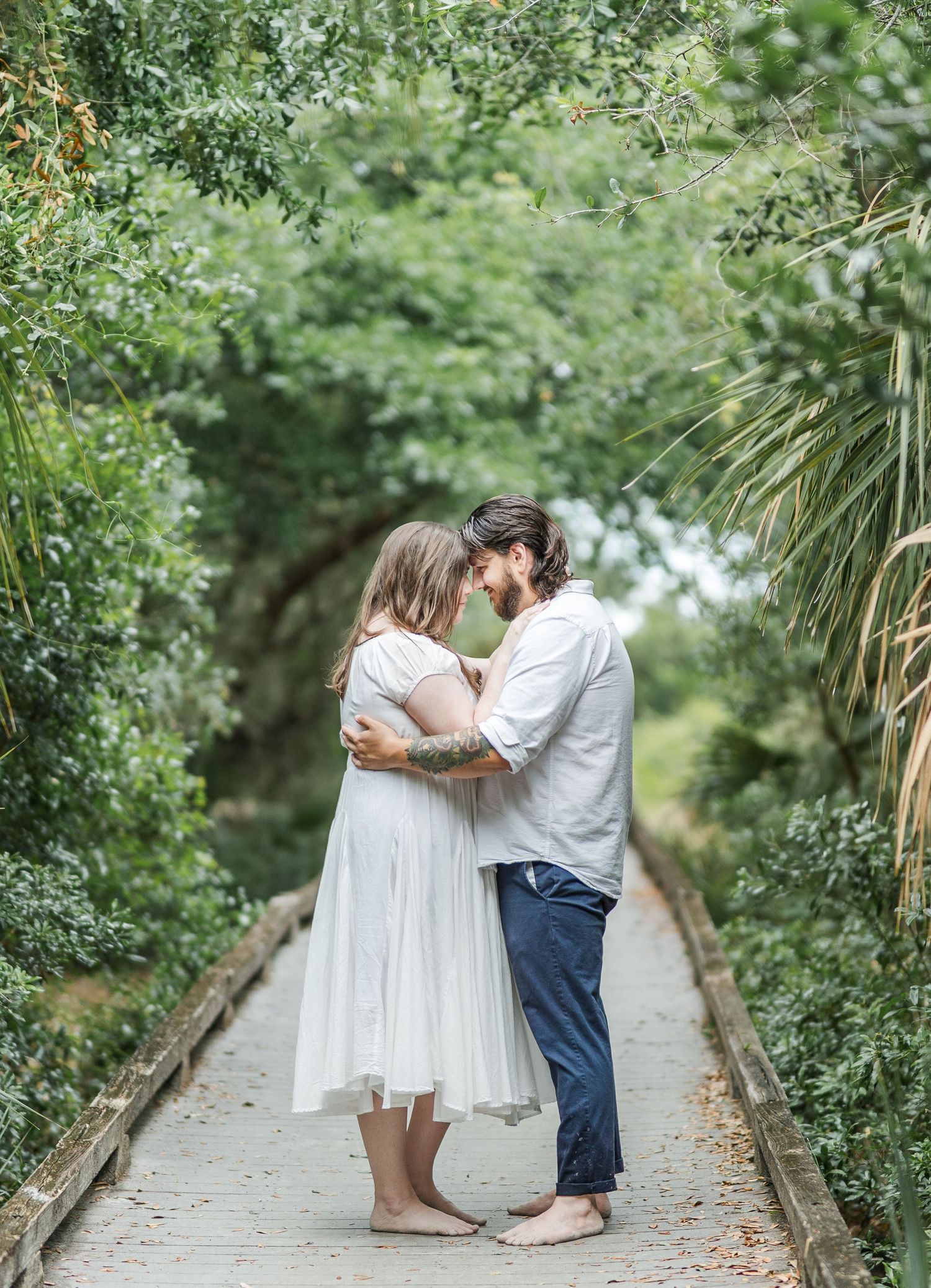 Intimate couple embraces on a scenic garden pathway surrounded by green foliage and palm leaves.
