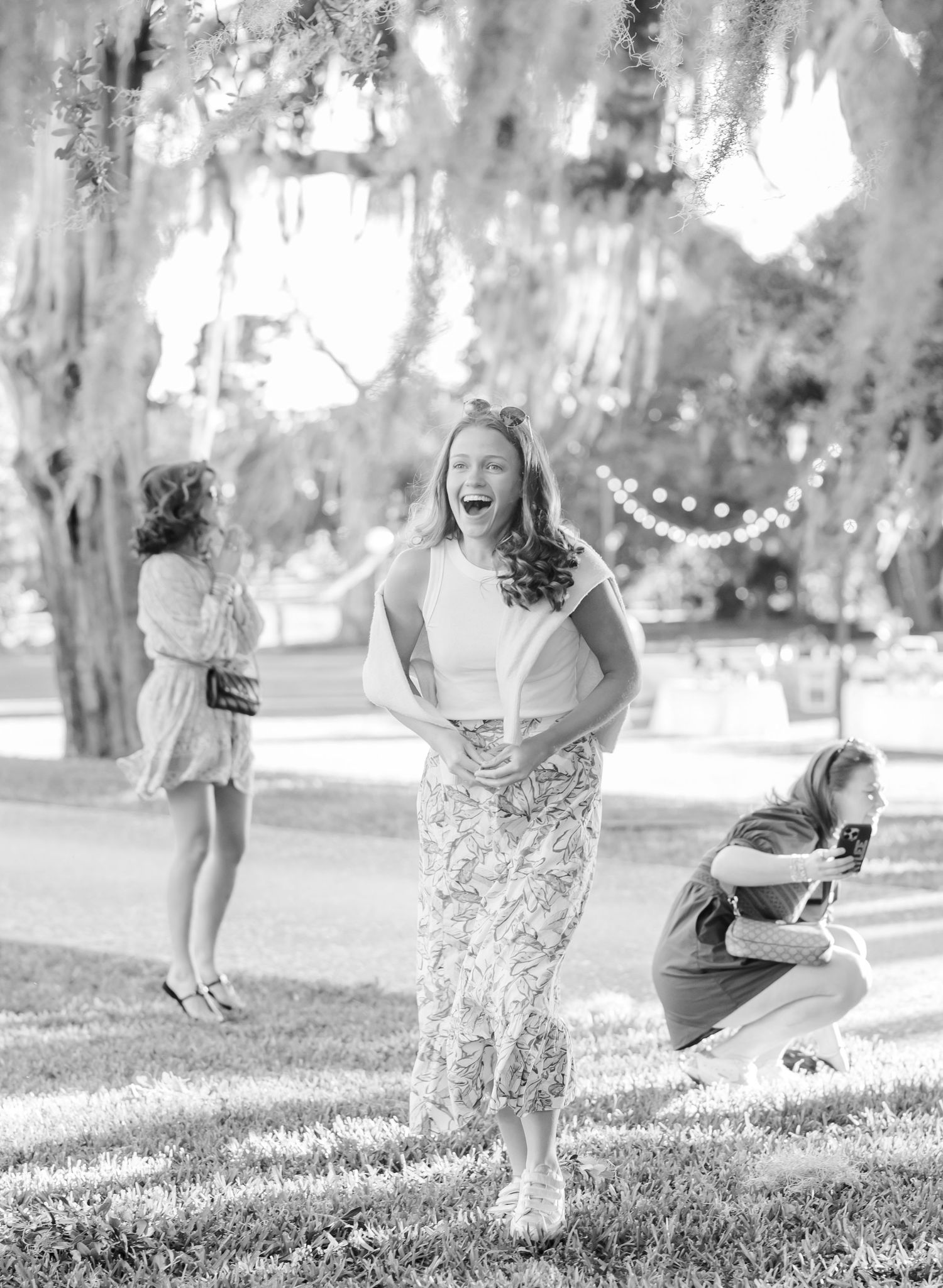 Black and white candid photo of people laughing and posing during an outdoor photoshoot in a park setting.