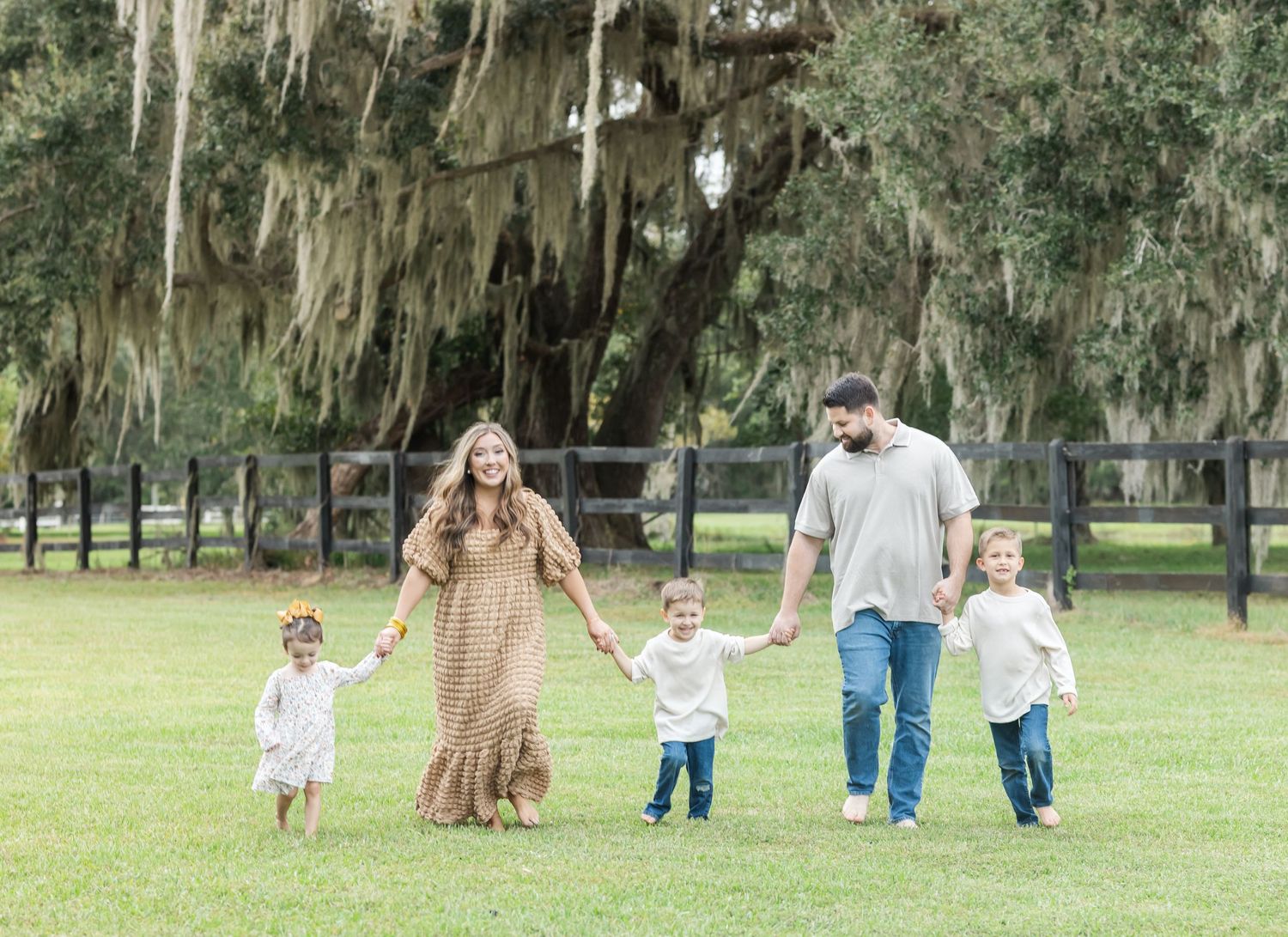 A family walks together under moss-draped oak trees in a serene park setting.