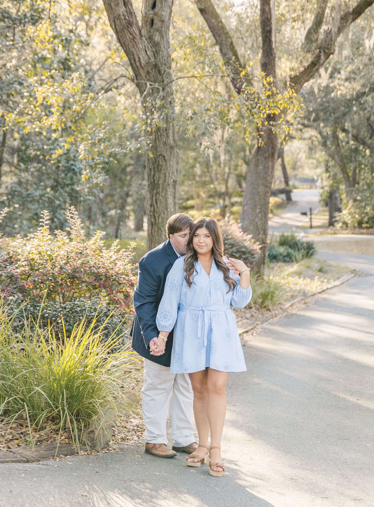 Couple embracing on a wooded path with ornamental grasses in the foreground.