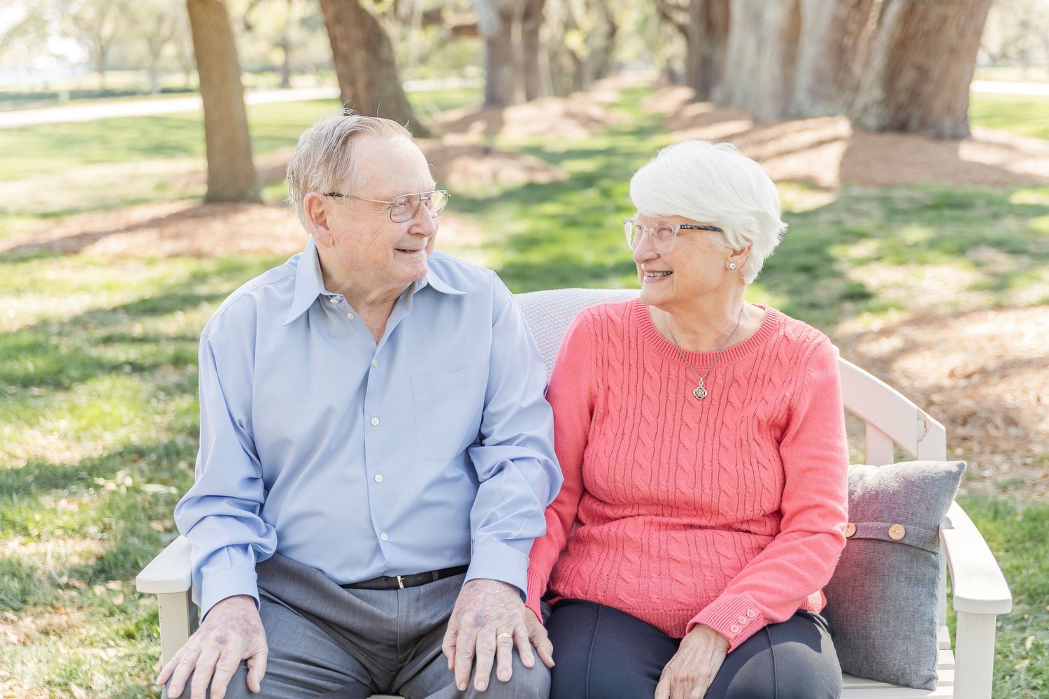 Senior couple shares an intimate moment while sitting on a bench in a wooded park.