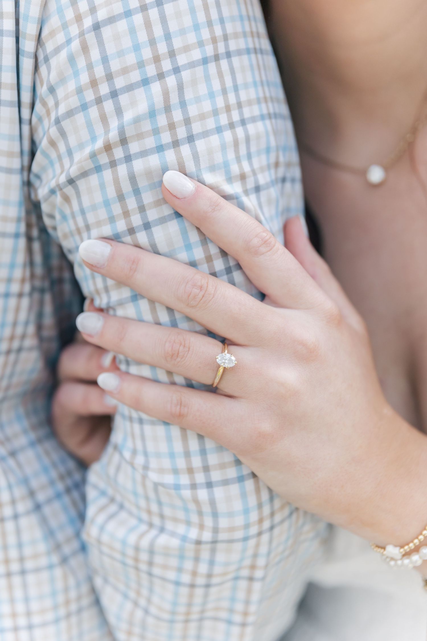 Detail shot of an engagement ring and golden bracelets against a plaid pattern.