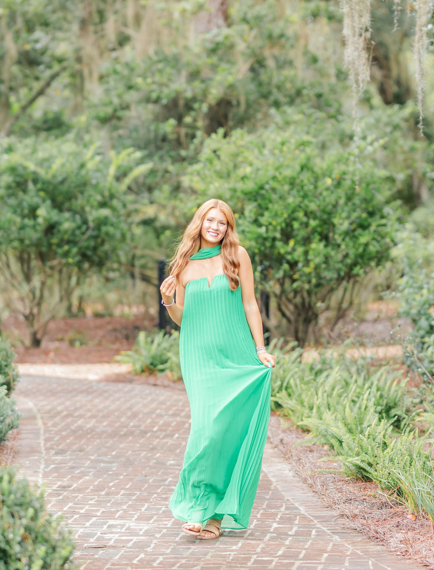 Movement sequence in a bright green pleated dress along a garden pathway with natural landscaping.