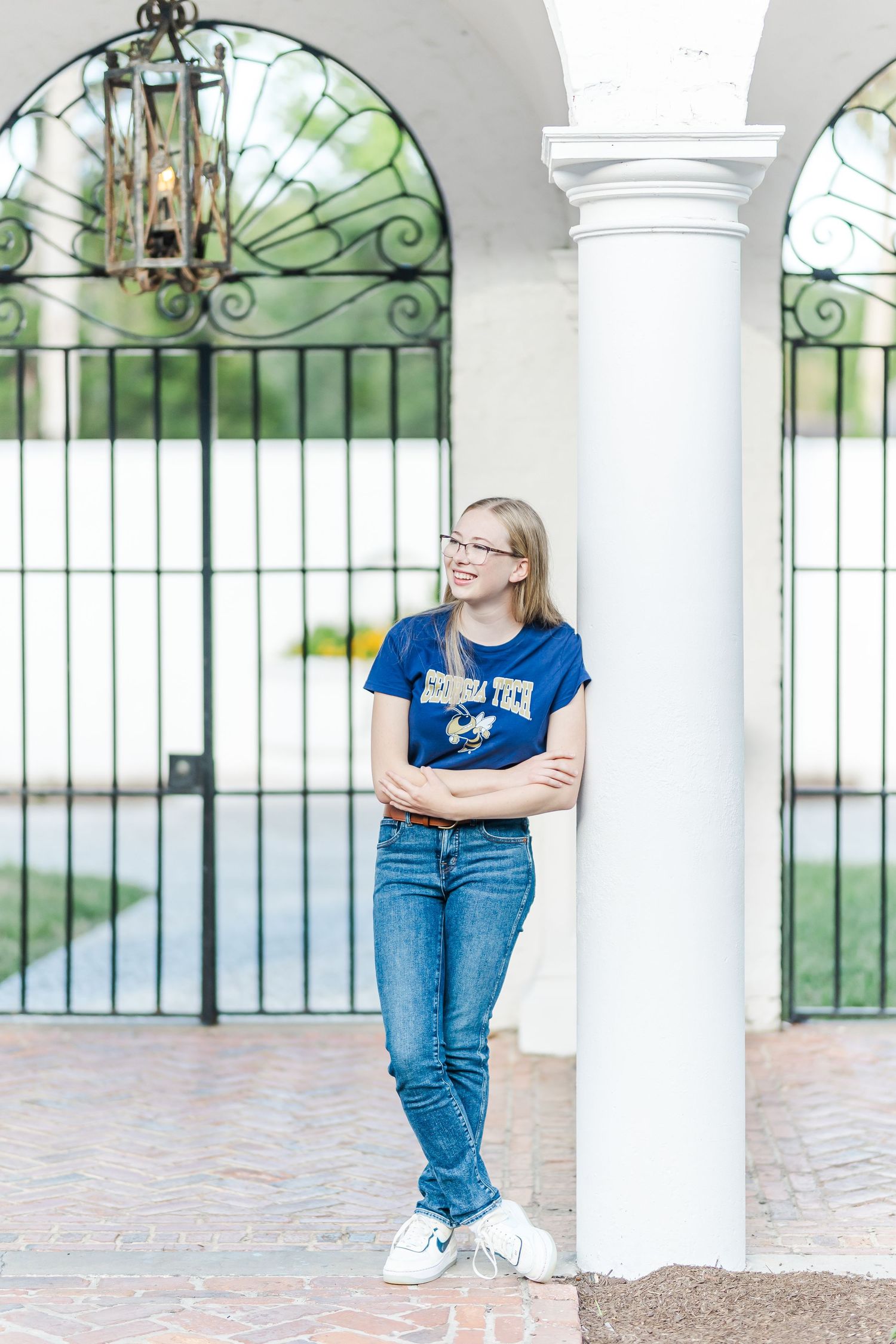 A person wearing jeans leans against white columns with ornate ironwork details in the background.