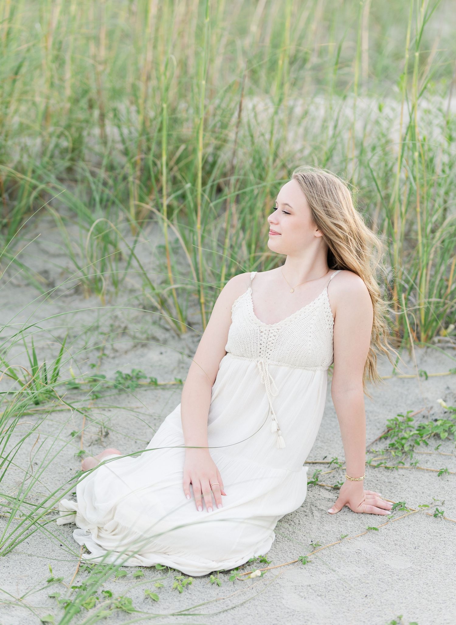Dreamy coastal photoshoot featuring flowing white dress among beach grass at sunset.