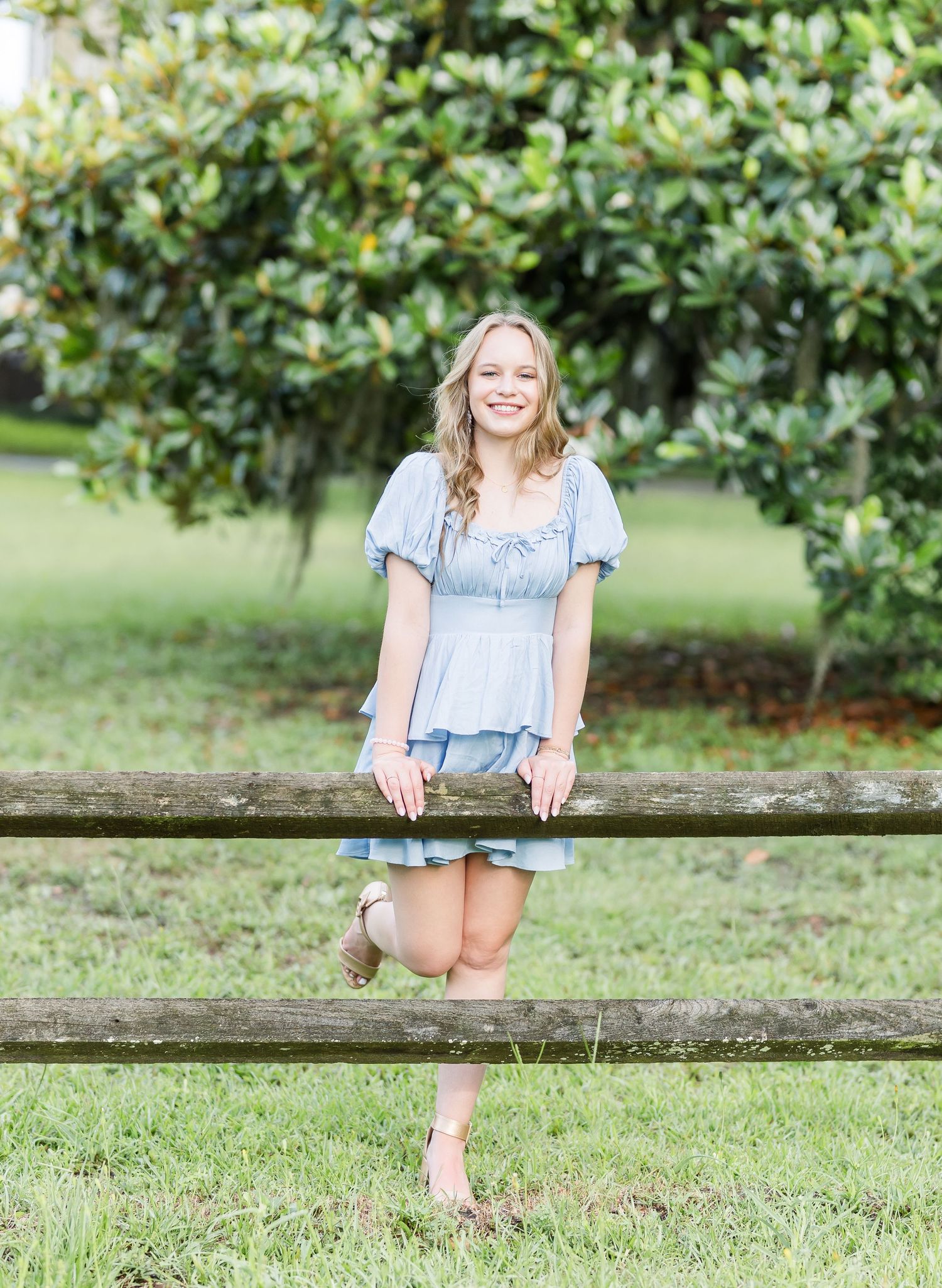A light blue puff sleeve dress worn while playfully posing by a wooden fence in a lush garden setting.