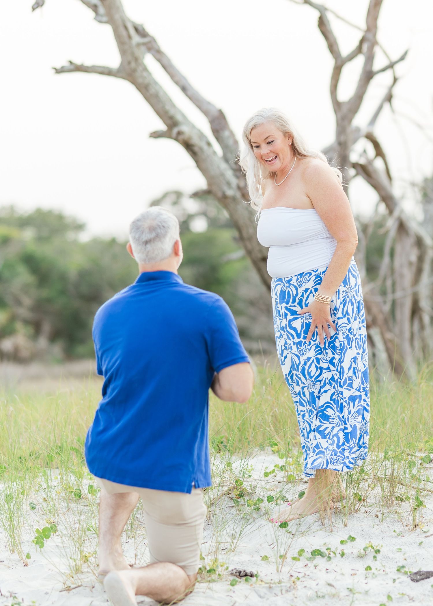 A couple shares a special moment as one kneels in front of the other on a sandy beach path.