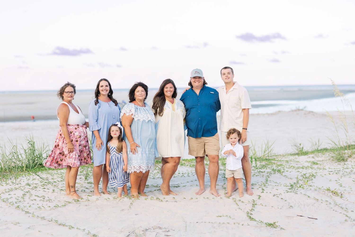 A group of people wearing white and blue outfits walk together on a sandy beach at sunset.