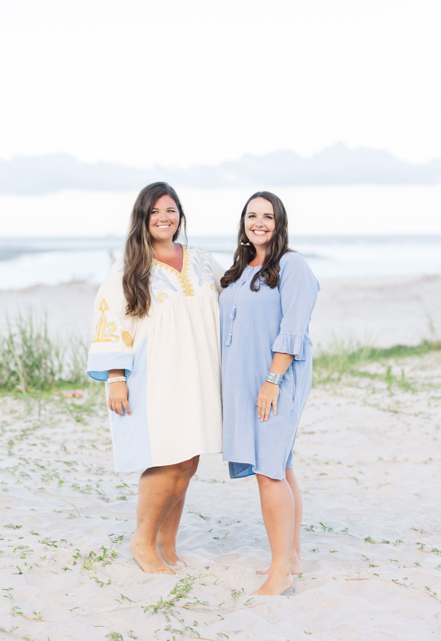 Friends sharing laughter while walking along the shoreline at sunset in casual summer attire.
