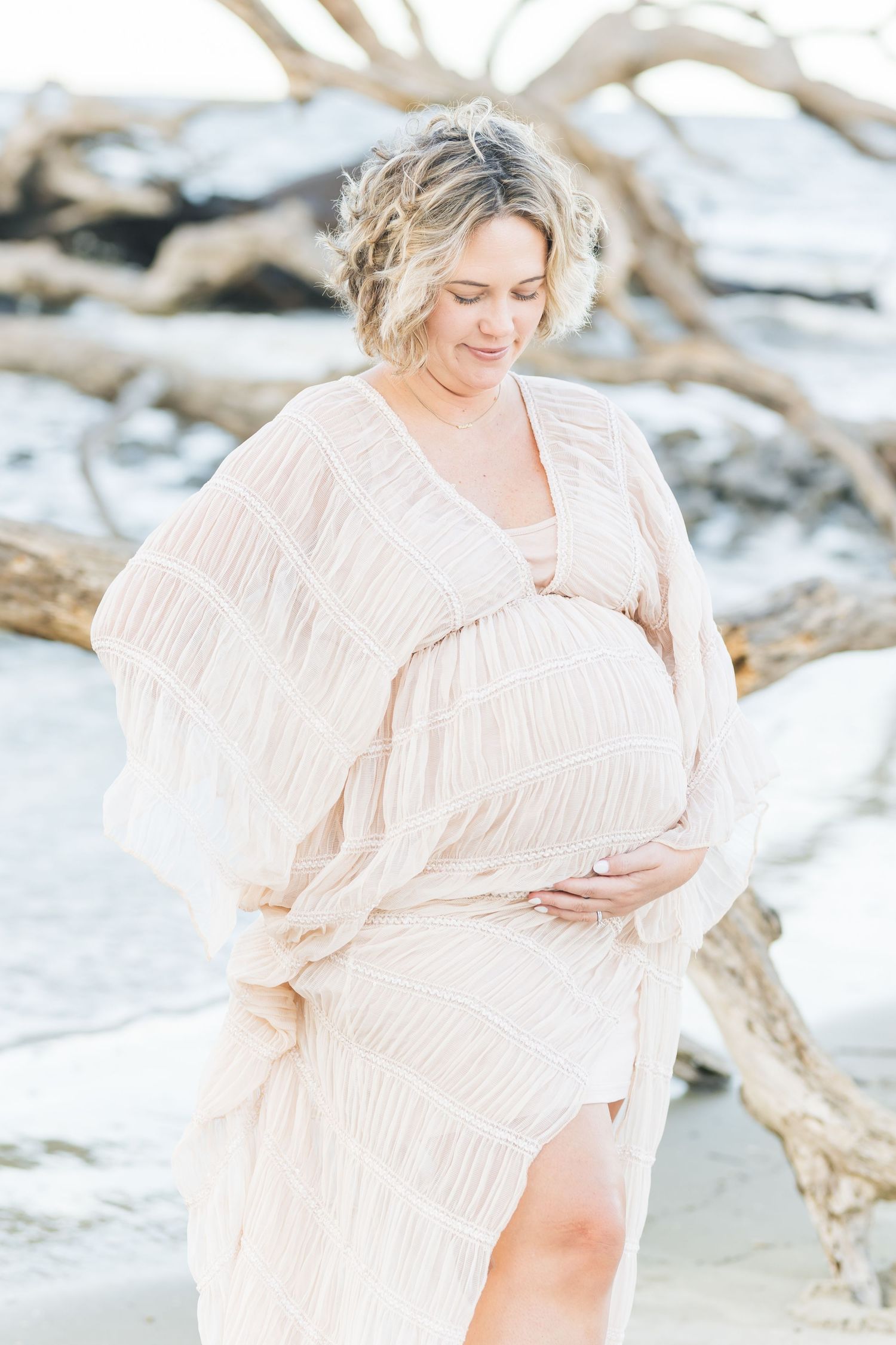 Soft pastel maternity photos captured on a serene beach with driftwood and gentle waves.