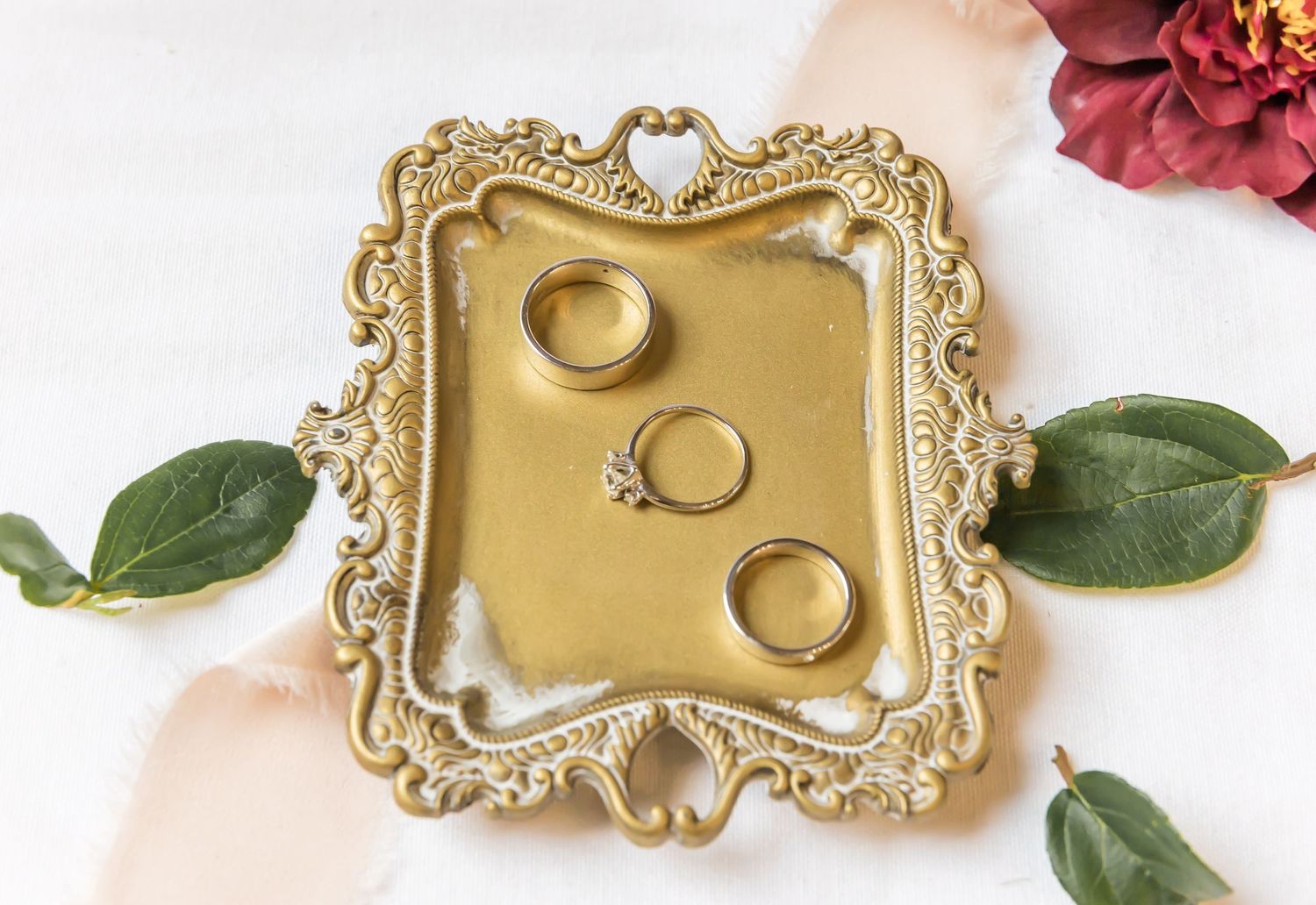 Wedding rings displayed on ornate gold vintage tray with green leaves.