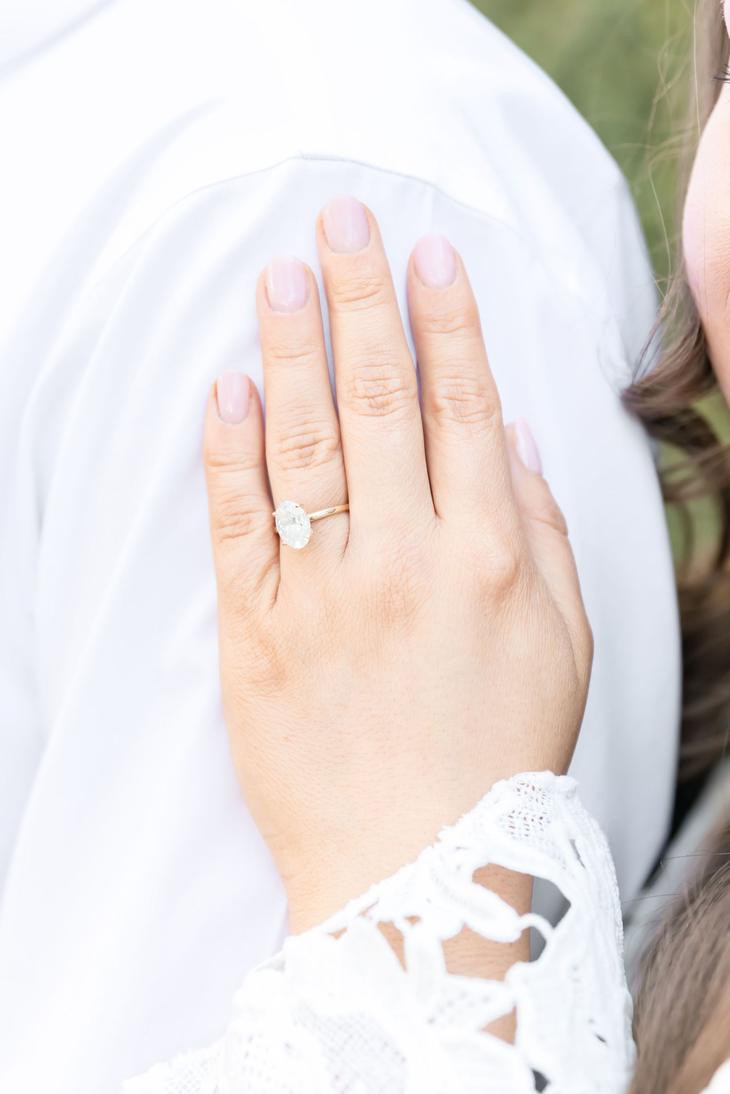 Close up of an engagement ring on a hand wearing white lace against a light background.
