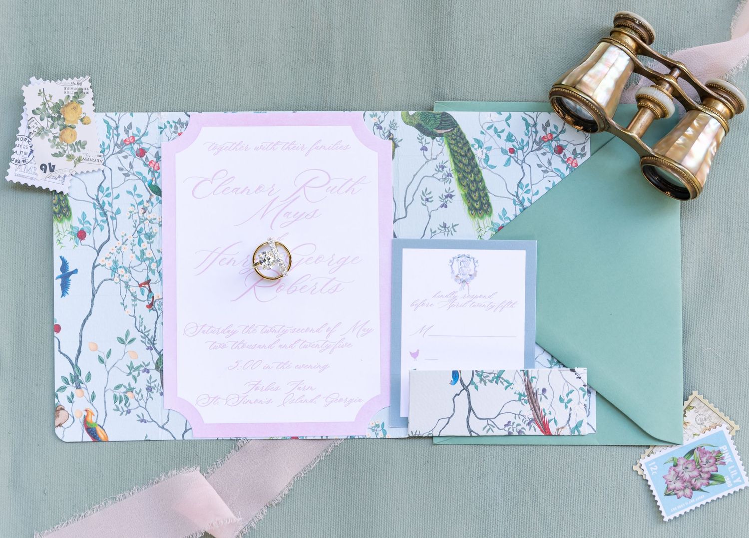 Wedding invitation suite with floral designs and antique opera glasses laid out on mint green background with pink accents.