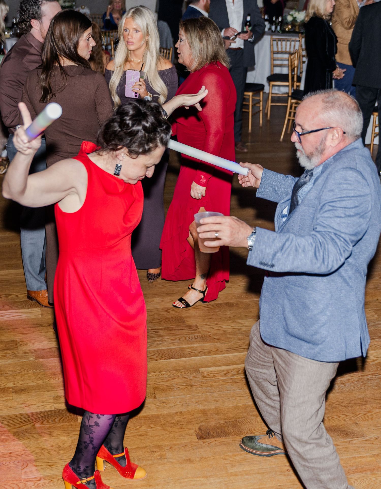 Wedding guests dance with glow sticks on the dance floor, woman in red dress leads the fun.
