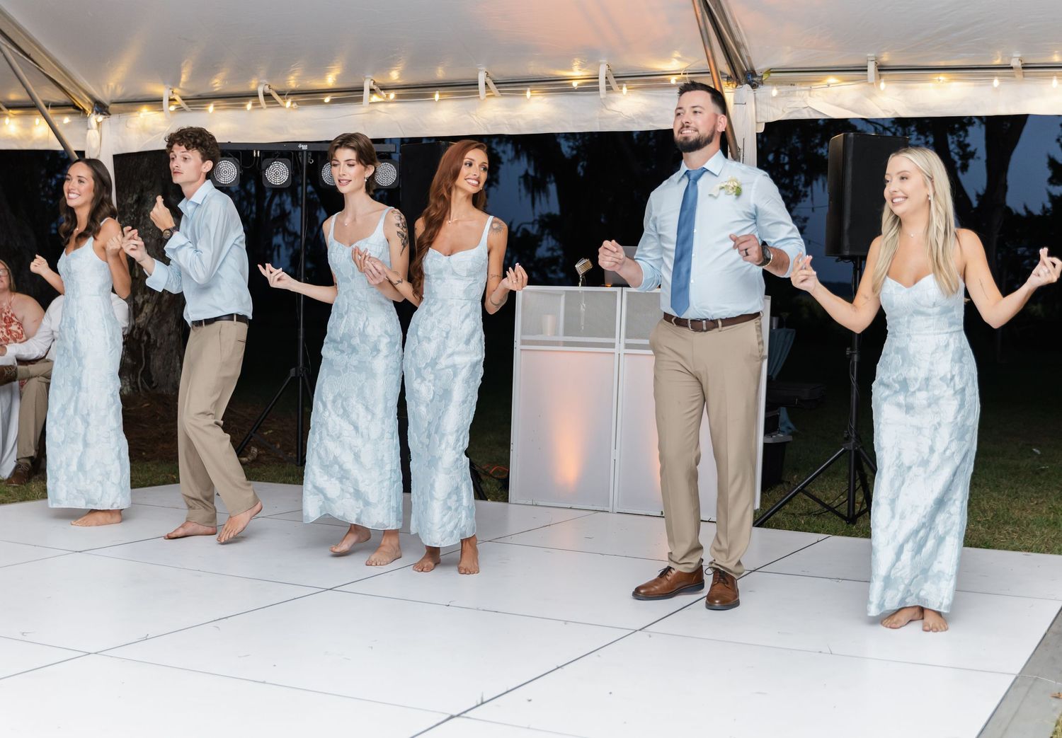 Wedding guests dancing and celebrating on a white dance floor under an outdoor tent at night.