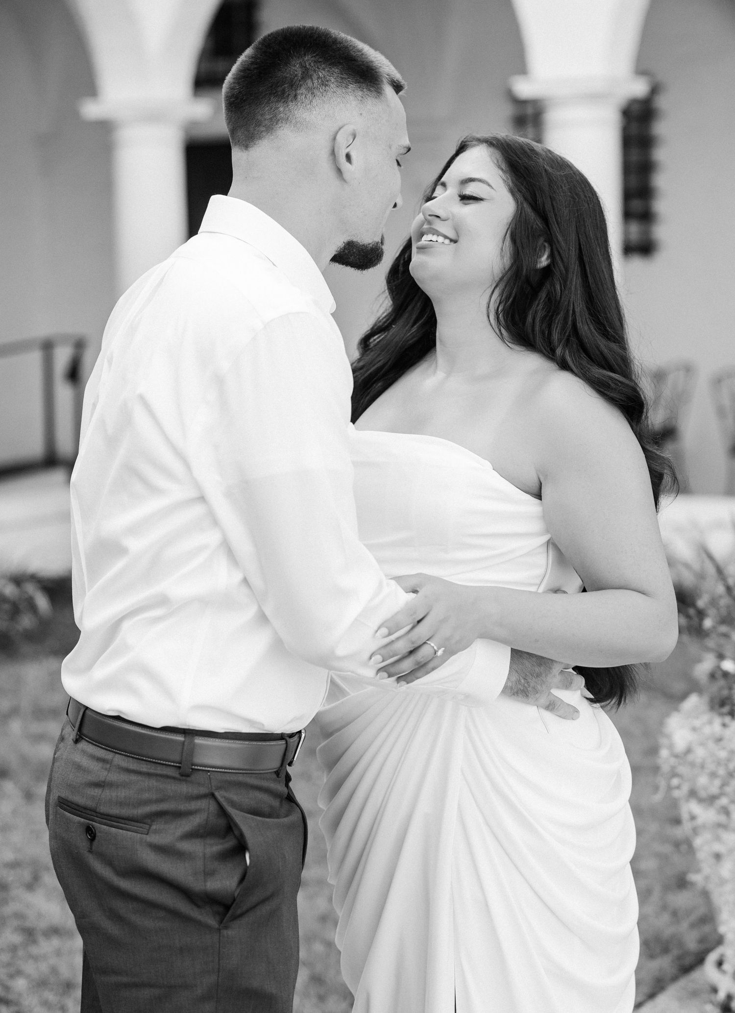 Black and white photo of a couple sharing a romantic moment, groom kissing bride's forehead as she smiles joyfully.