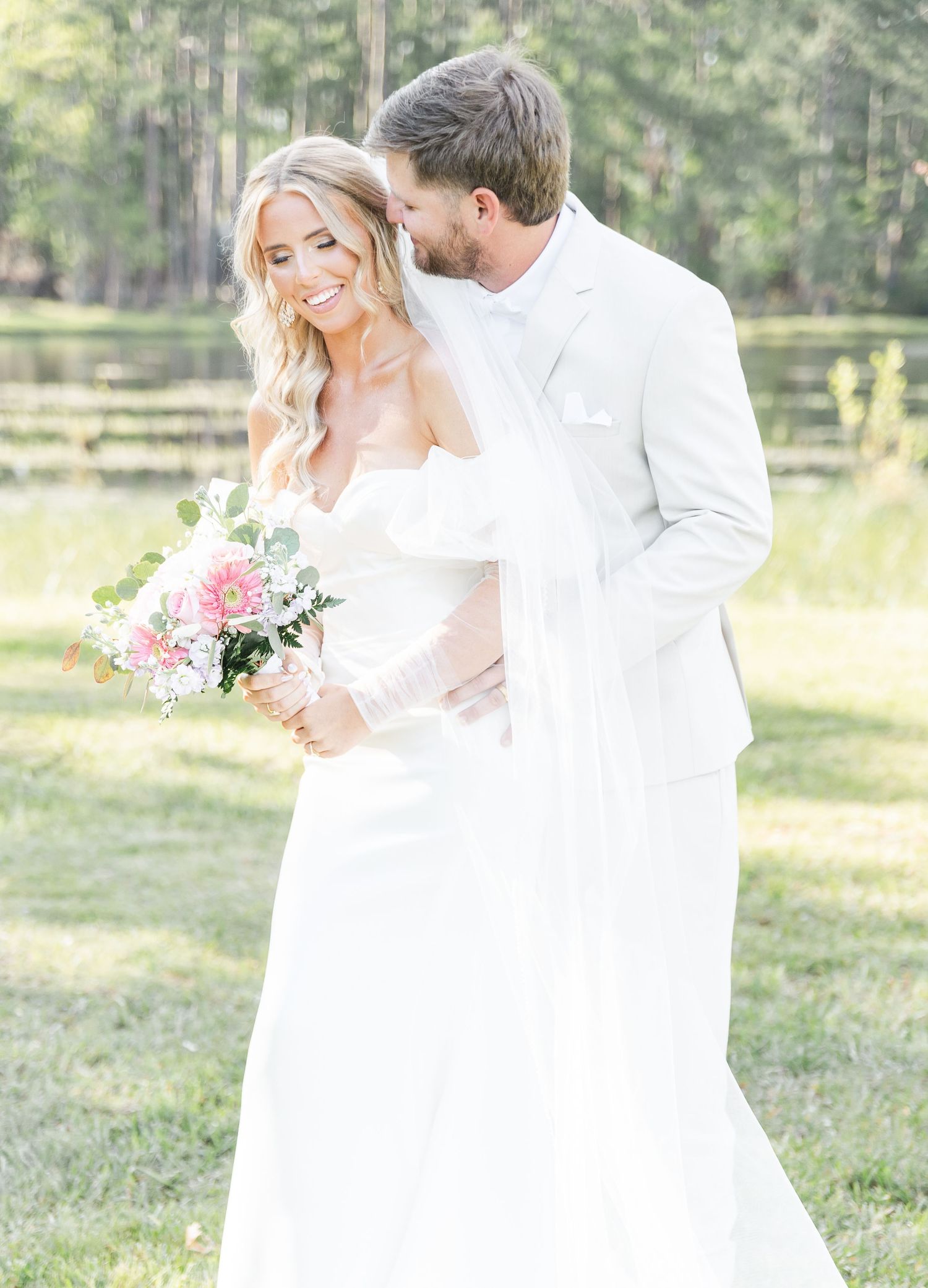 Elegant outdoor wedding portrait with couple in white sharing intimate moment by scenic pond.