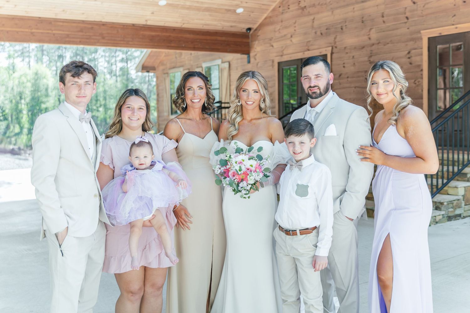 Wedding party in coordinated white and cream outfits poses together at rustic venue.