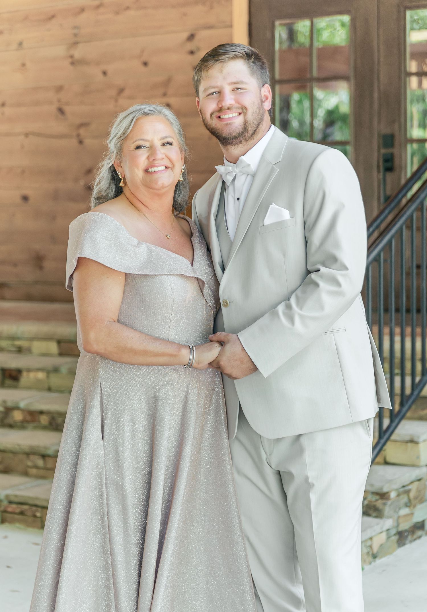 Two people in formal grey attire share a moment at a wooden venue.
