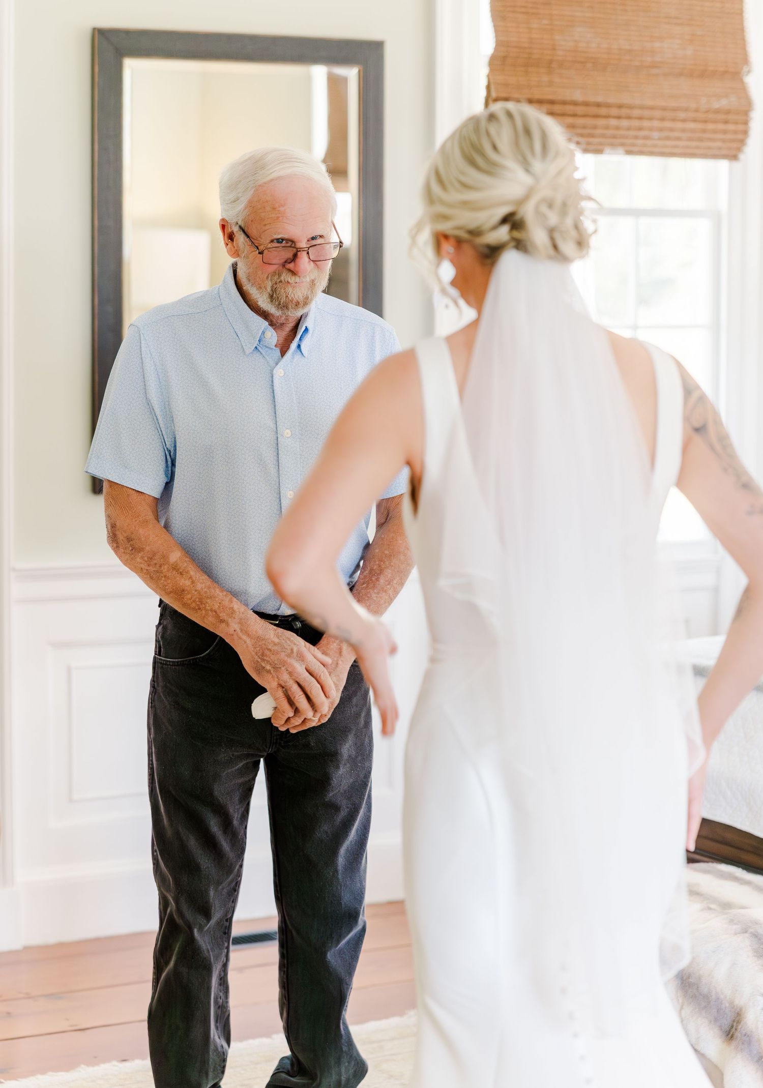 Emotional father sees bride daughter in wedding dress for the first time during a touching first look moment indoors.