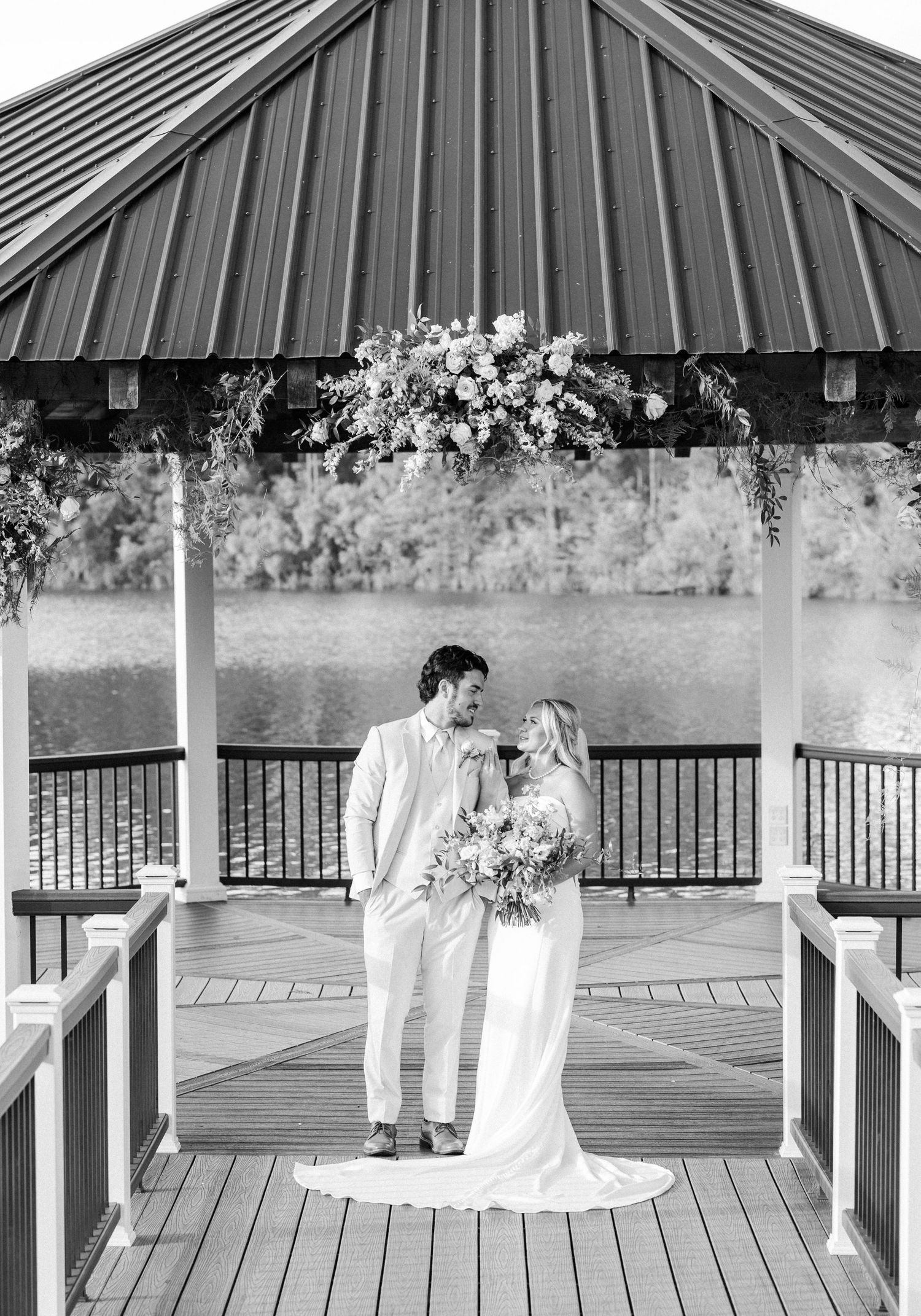 Black and white photo of bride and groom sharing a moment in a lakeside gazebo.