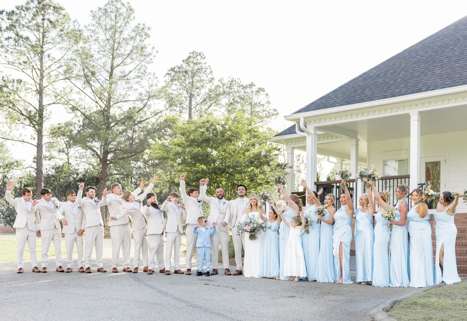 Wedding party celebrates in light blue and white attire outside a white pavilion.