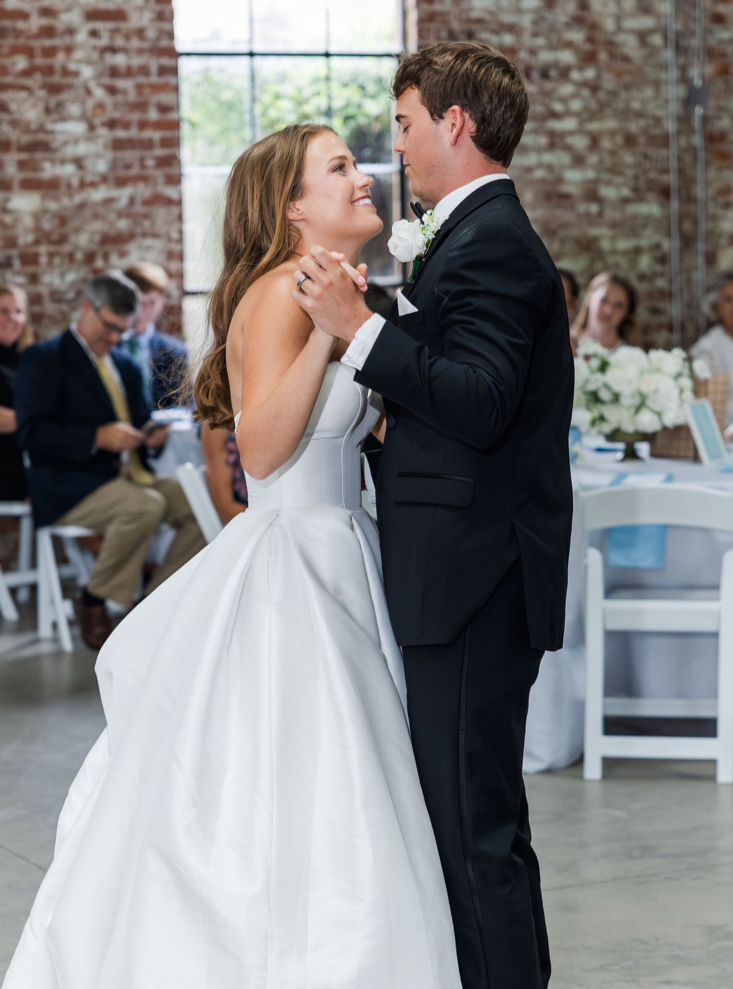 Bride and groom share romantic first dance in rustic brick-walled wedding reception venue.