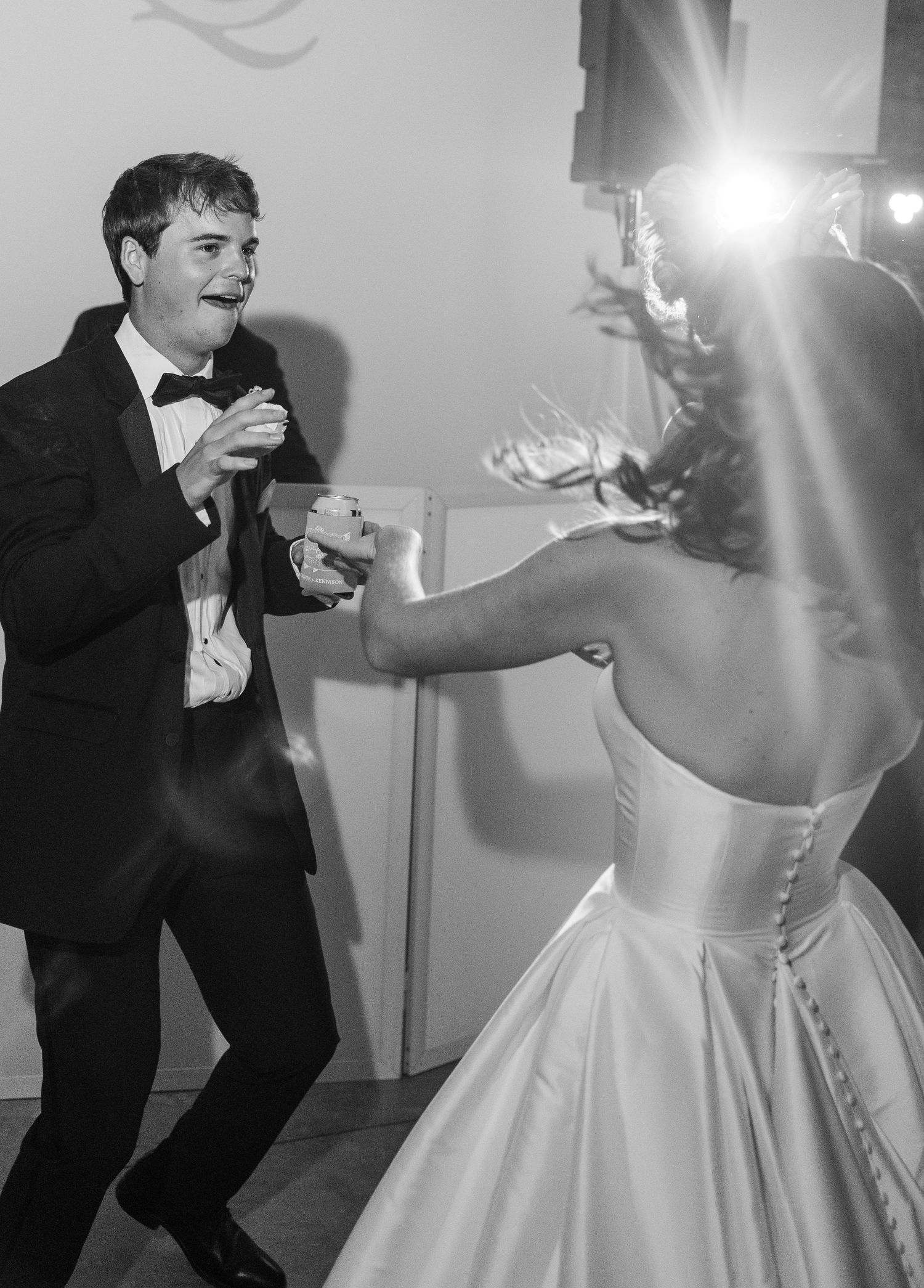 Groom in tuxedo dances energetically with bride in ballgown at wedding reception.