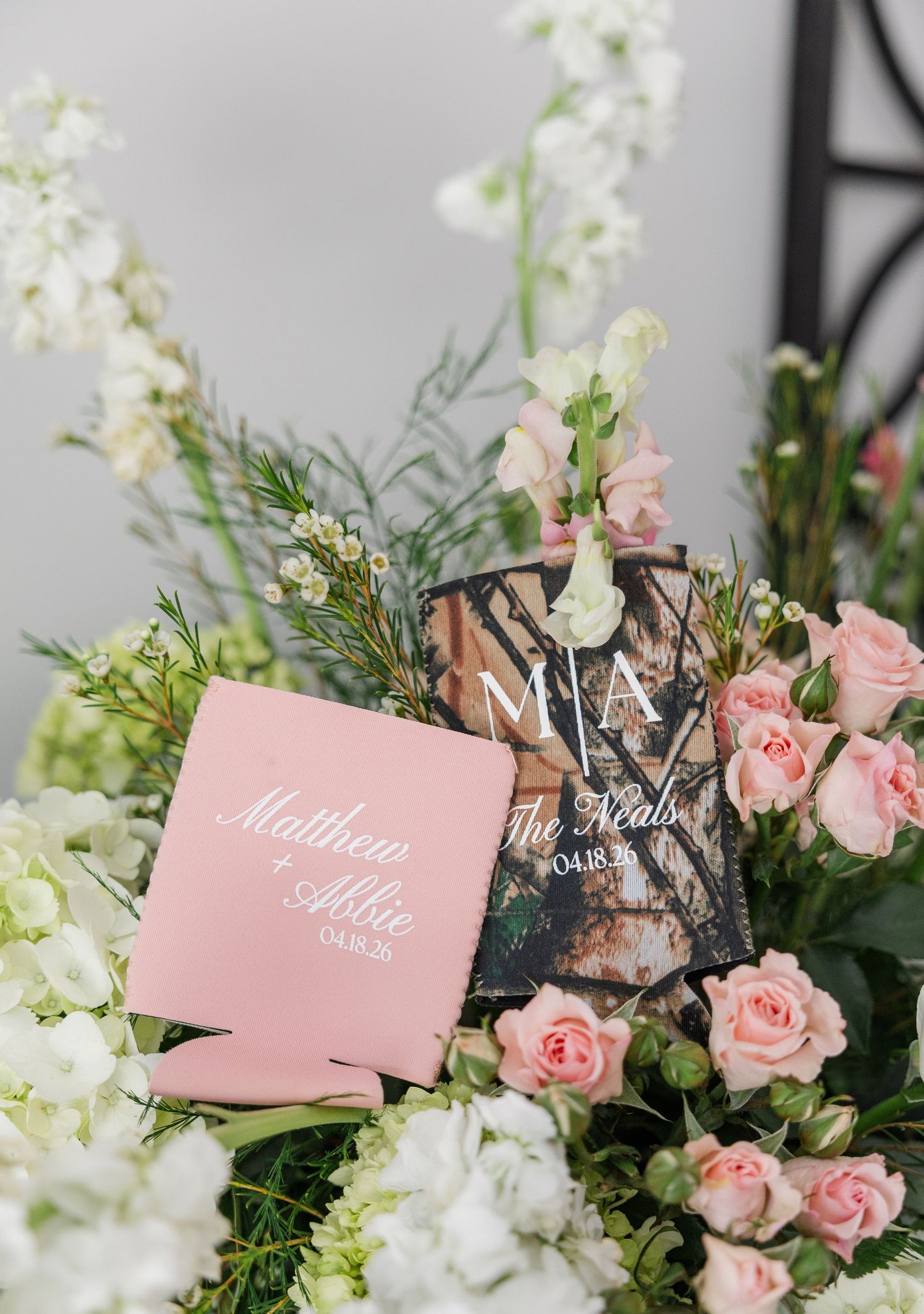 Personalized pink and camo wedding koozies for Matthew and Abbie Neal surrounded by pink roses and white flowers.
