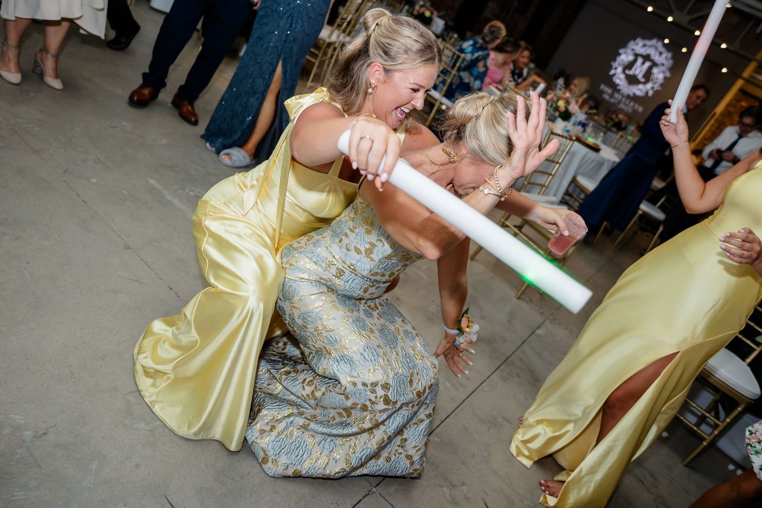 People dancing and celebrating at a wedding reception in formal attire with yellow bridesmaid dresses visible.