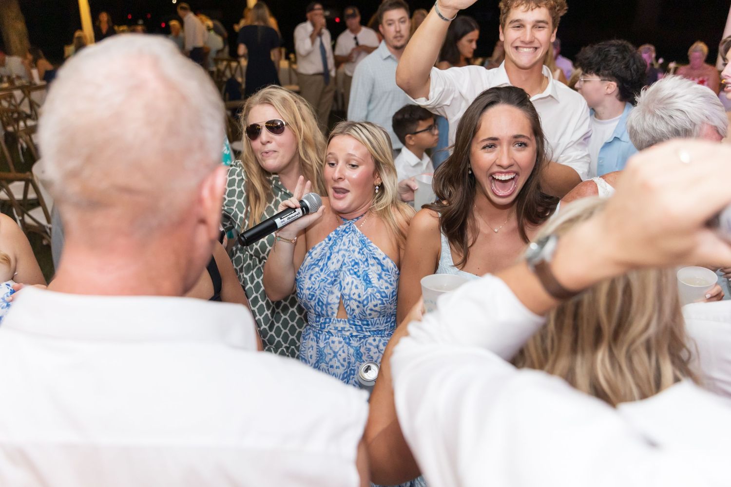 Guests mingling and dancing at a lively outdoor wedding reception under a tent.