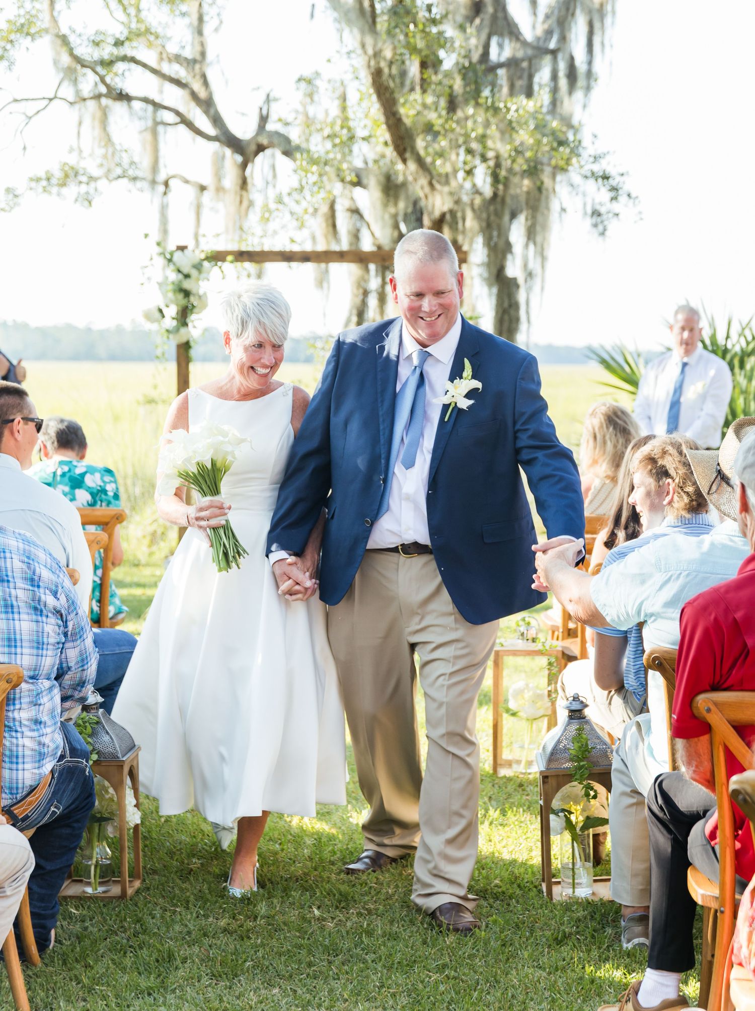 Wedding guests mingle and socialize during an outdoor reception under Spanish moss-draped trees.