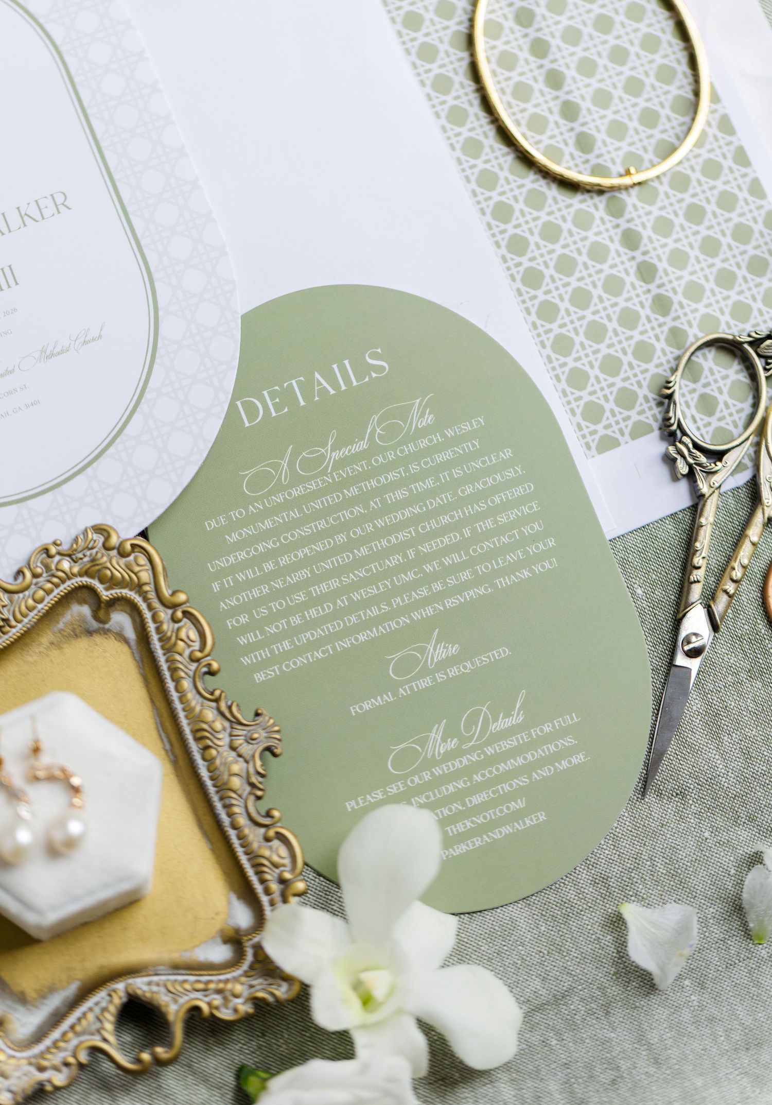 Elegant wedding invitation details in sage green and gold with ornate decorative elements and white floral accents.