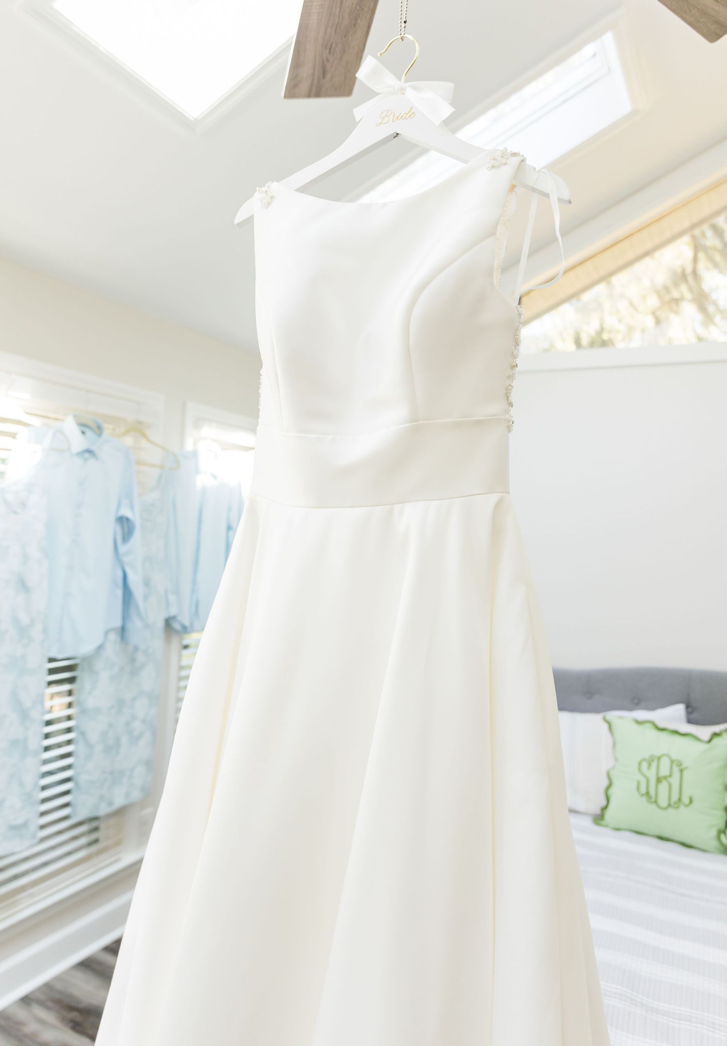 An elegant white wedding dress with a one-shoulder design hangs on display in a bright room with soft lighting.