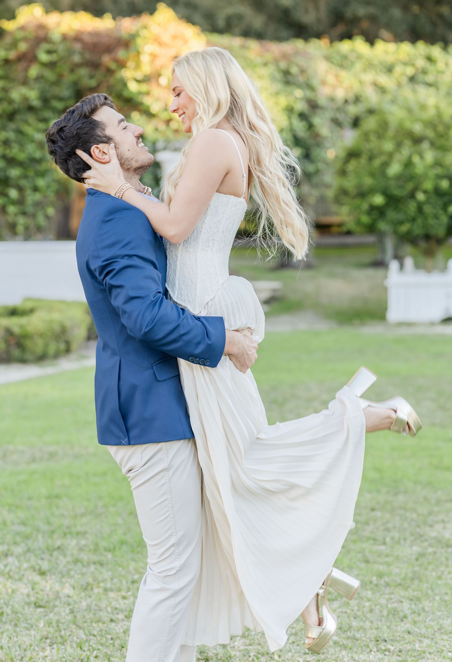 A couple shares a joyful dance moment on a grassy lawn during their engagement session.