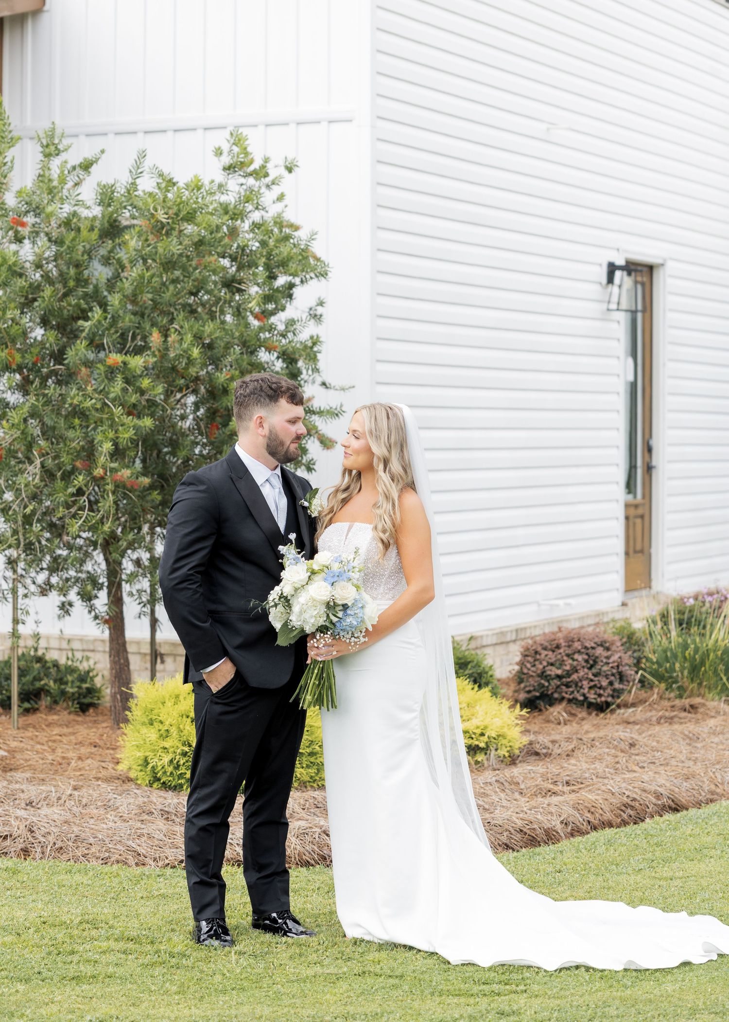 Bride and groom sharing romantic first look outside white barn wedding venue on sunny day.