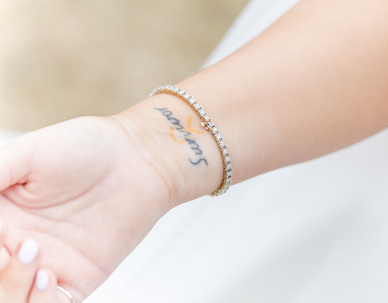 Close-up of a diamond tennis bracelet on a wrist with a cursive script tattoo.