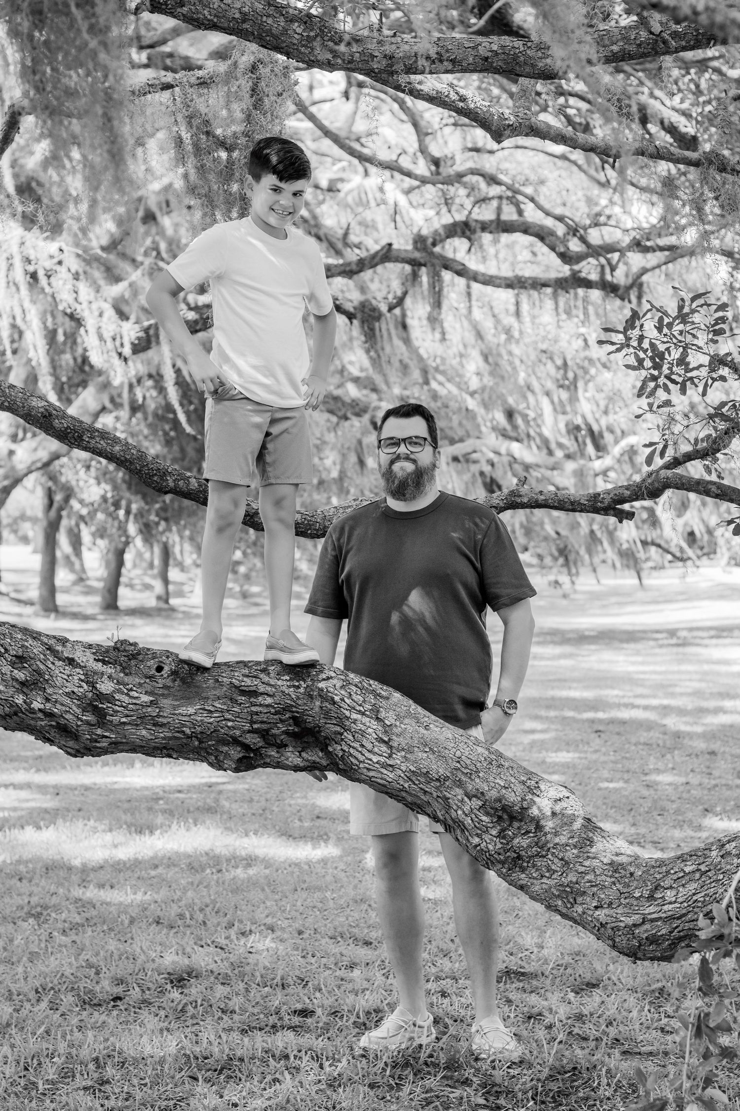 Two people pose near a large curved tree branch in a black and white outdoor portrait.