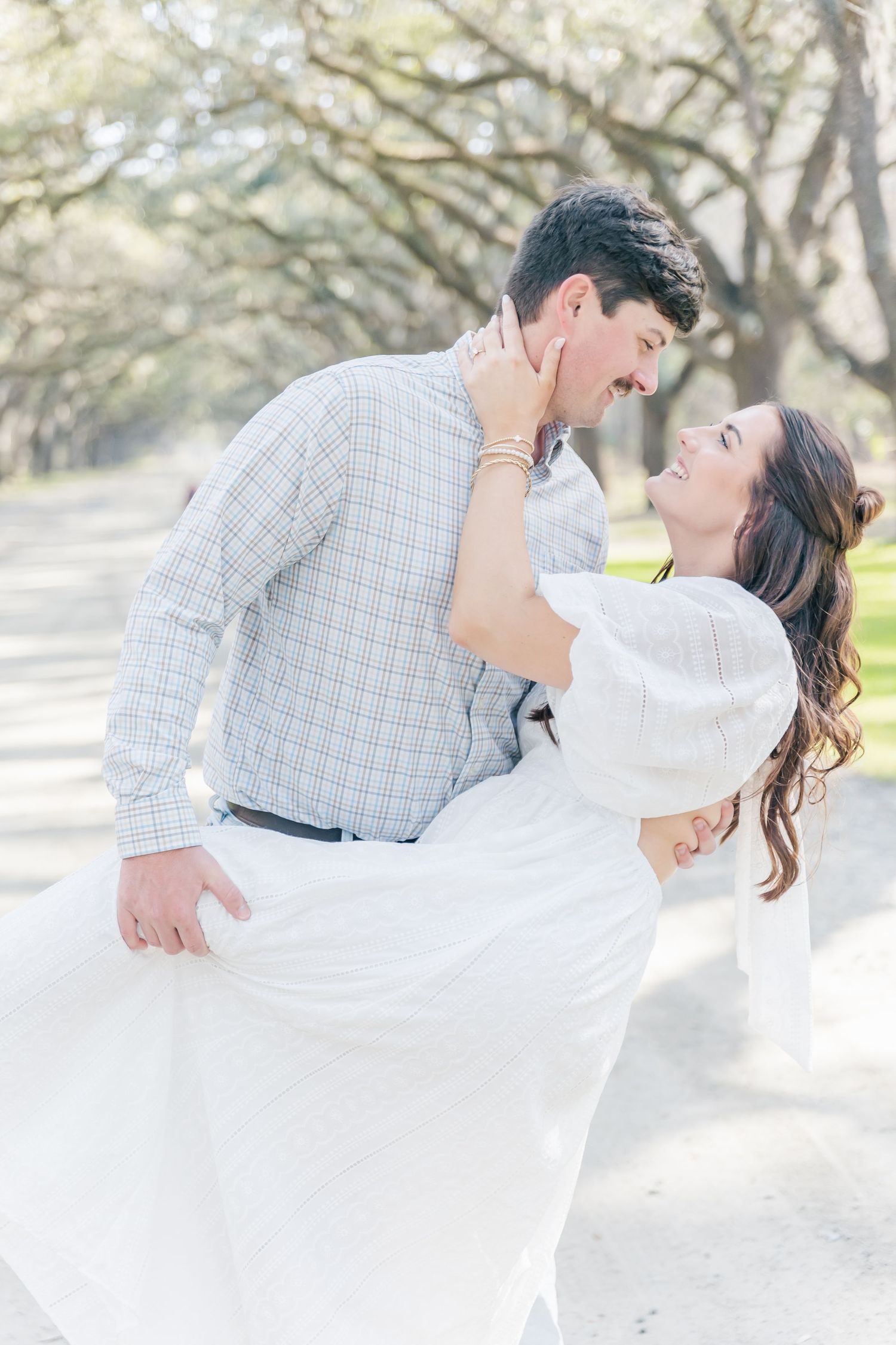 A couple share an intimate moment beneath an arched canopy of trees during their photoshoot.
