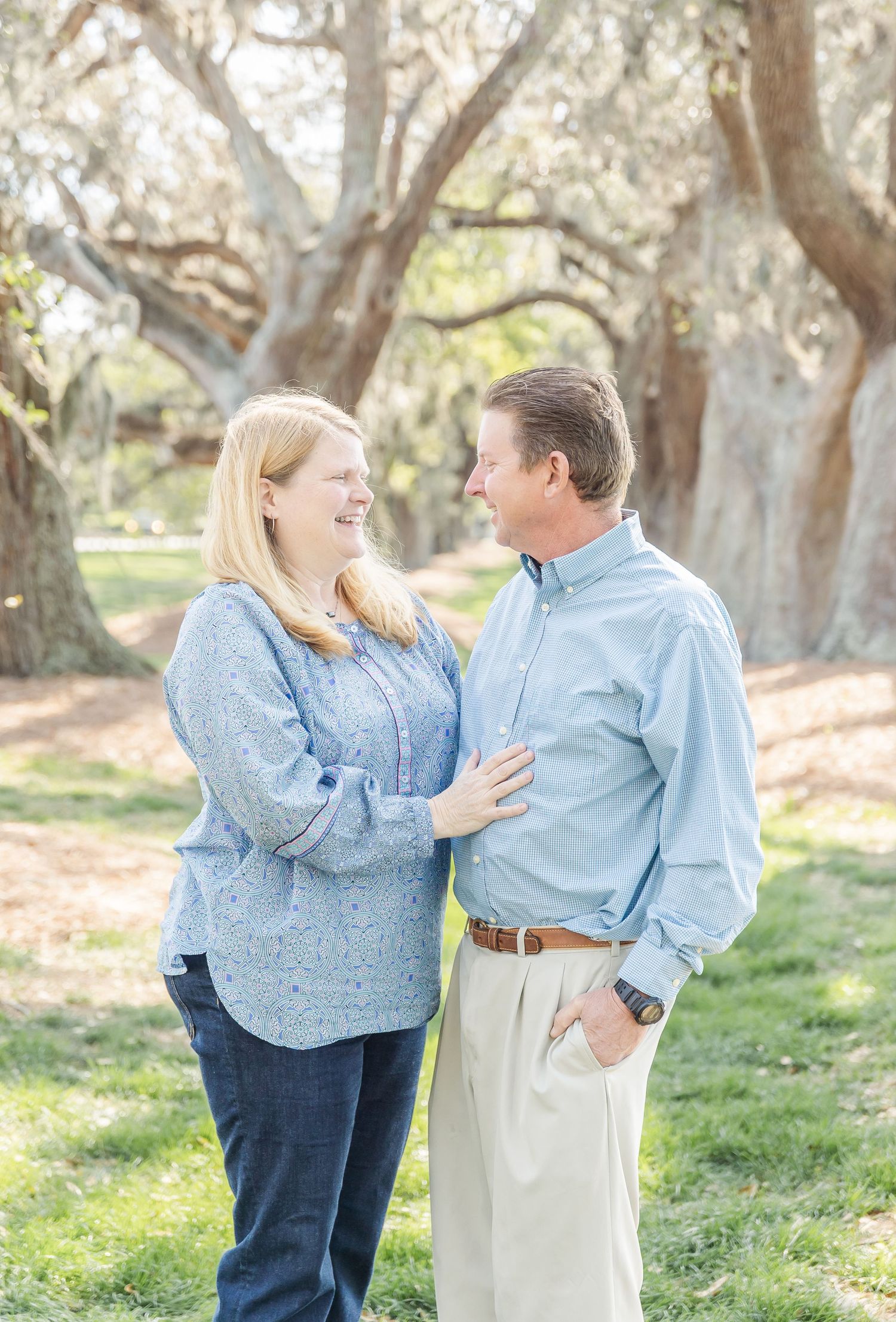 Couple in matching blue shirts share a happy moment together under a canopy of oak trees.