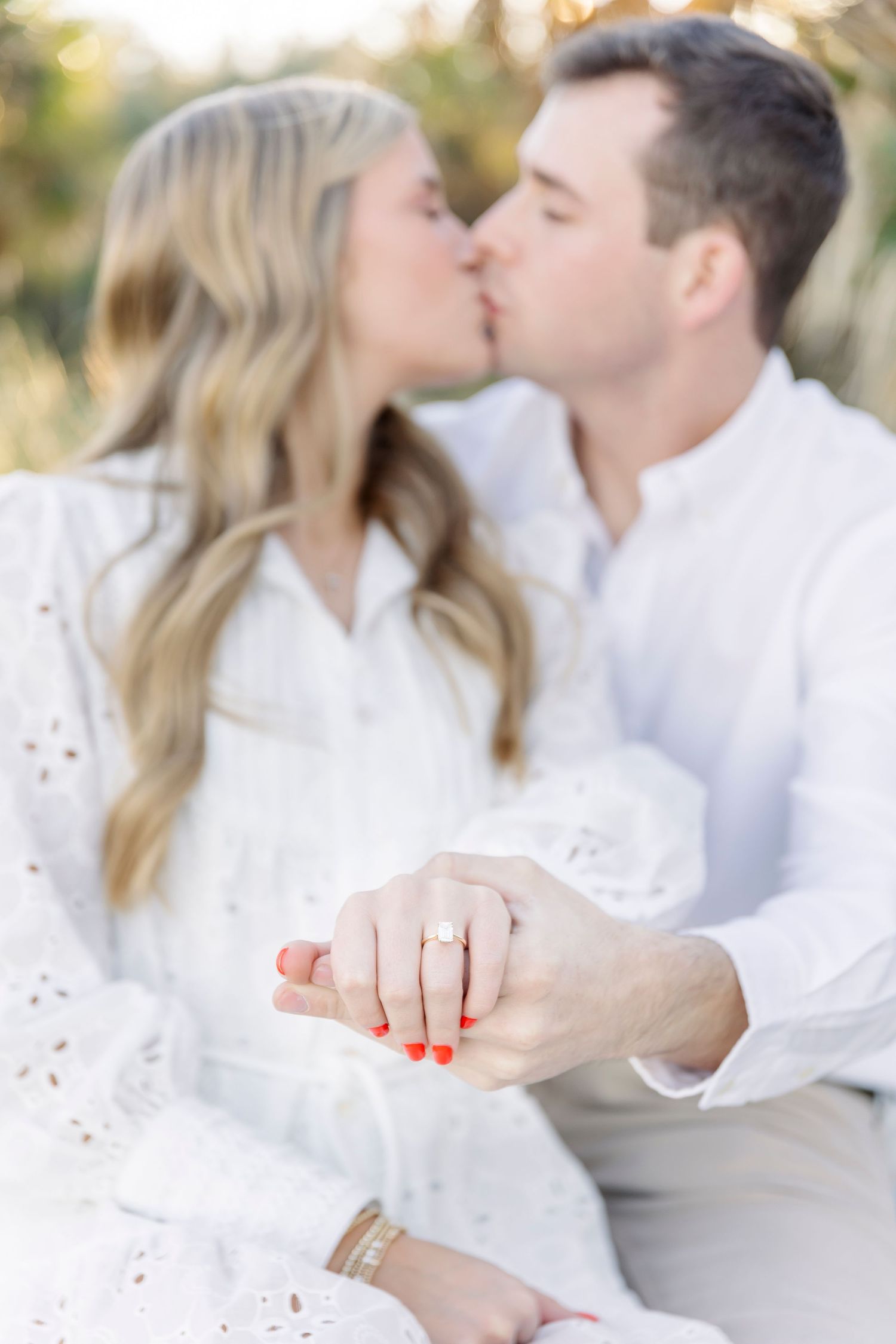 Romantic beach engagement photo showing ring while couple shares a kiss.