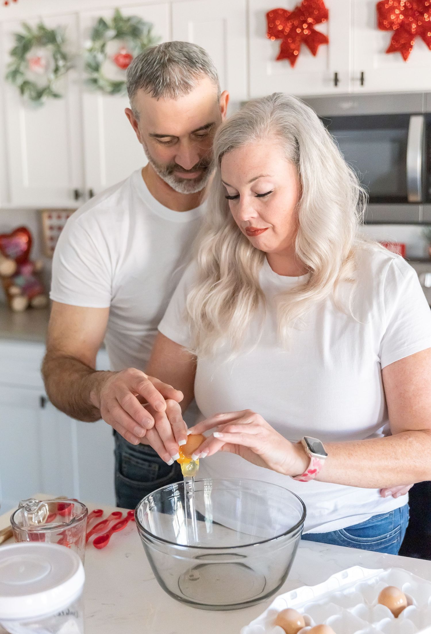 Happy couple works together cracking eggs into mixing bowl while holiday baking.