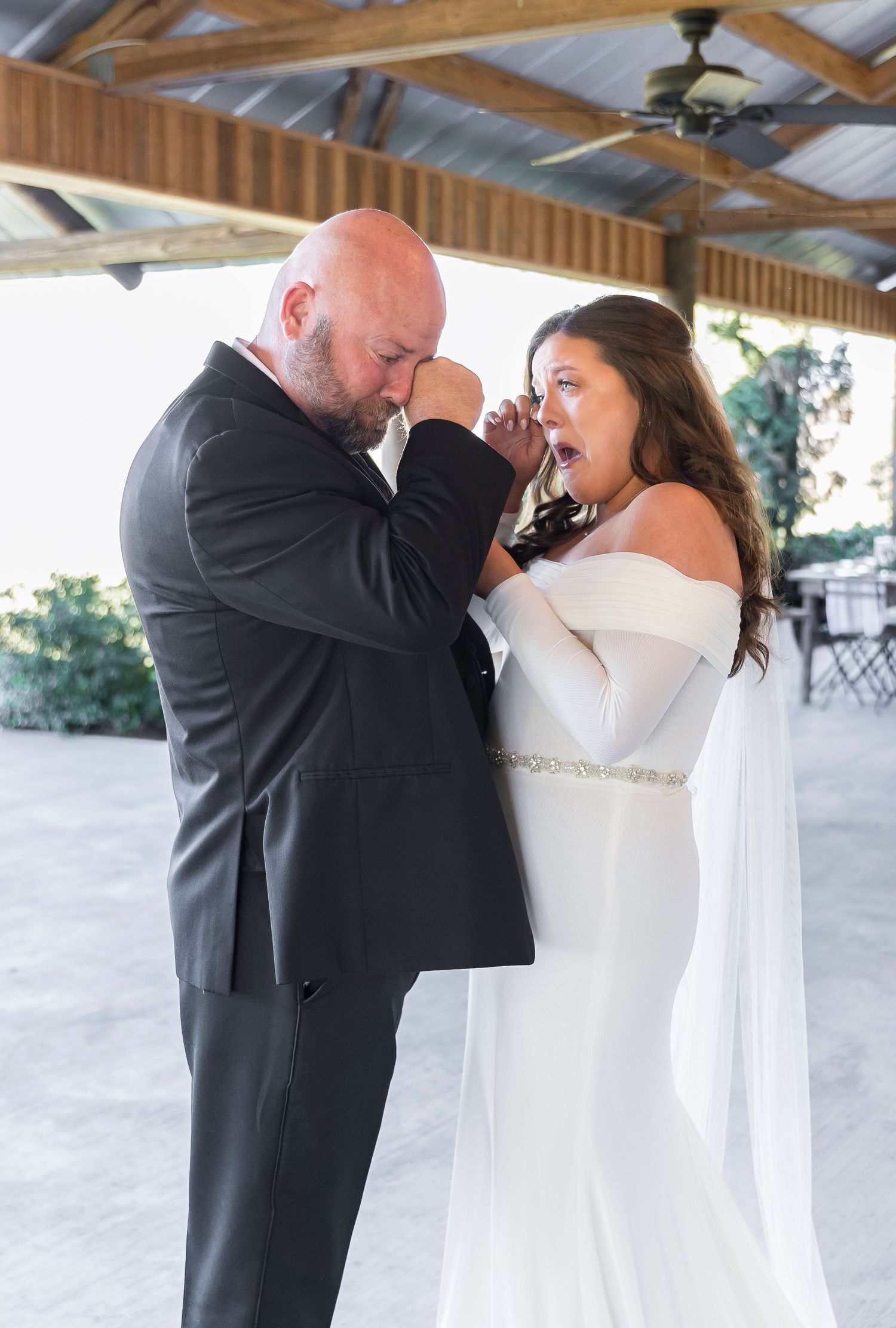 An emotional moment shared between couple in wedding attire under wooden pavilion.