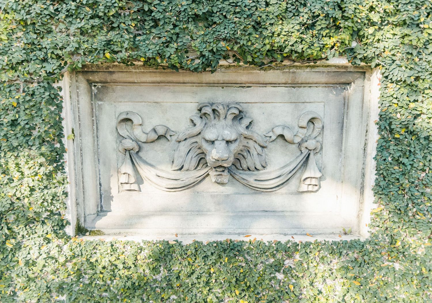 An ornate stone relief carving features cherubs and garland designs framed by ivy.