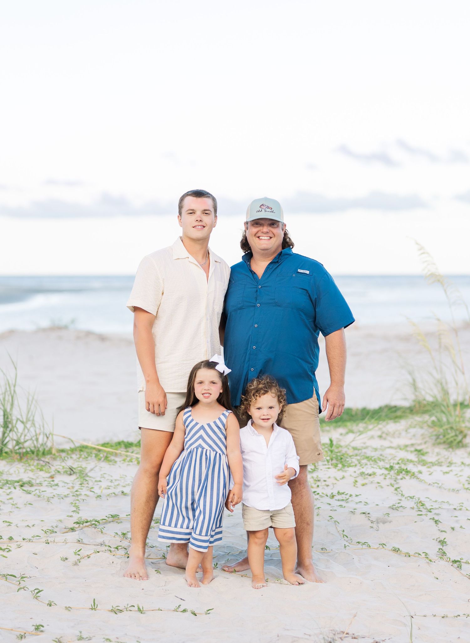 Group gathered on a beach with gentle waves and coastal vegetation visible in the distance.