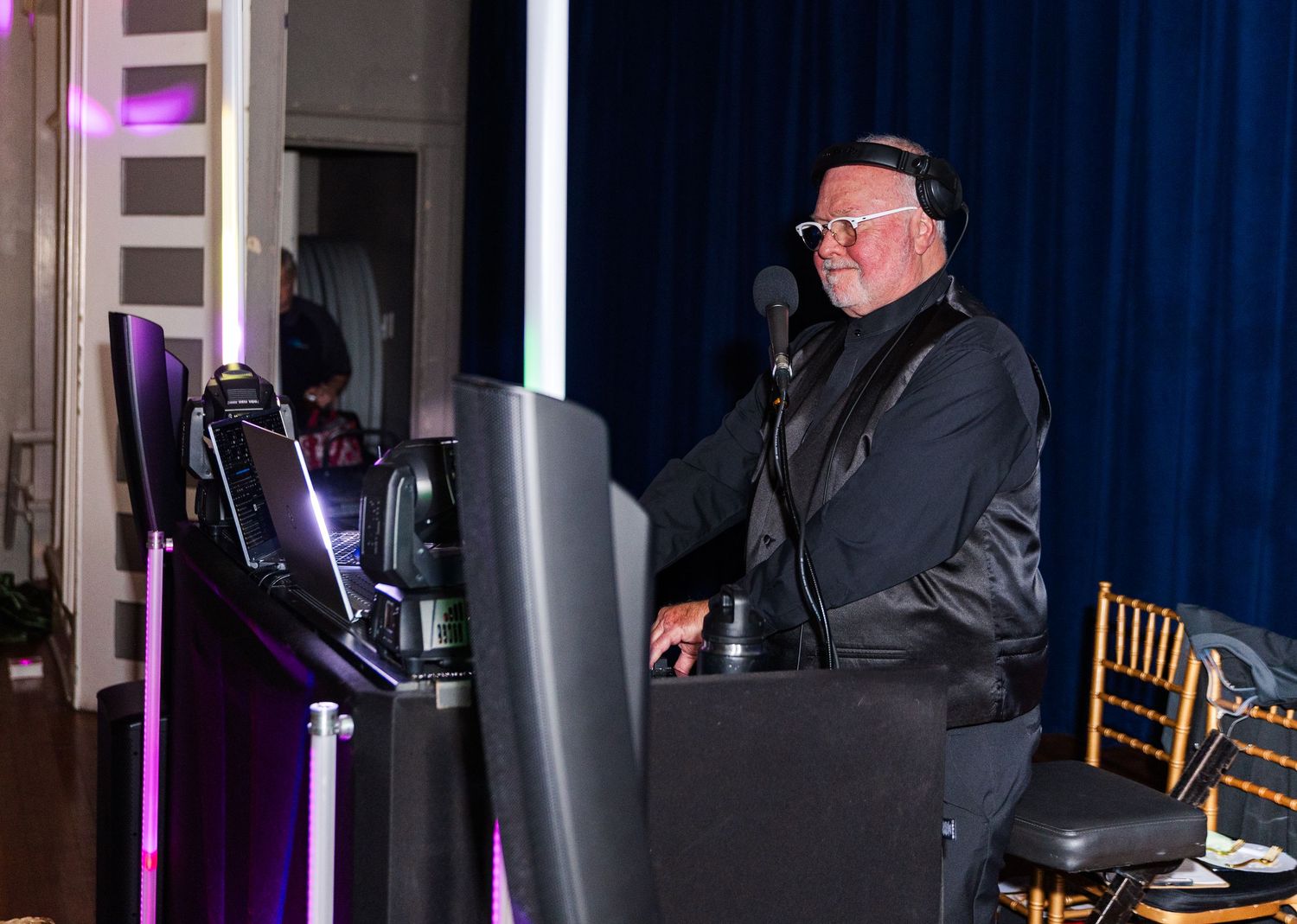 DJ performing at a wedding reception with purple and blue lighting in the background.