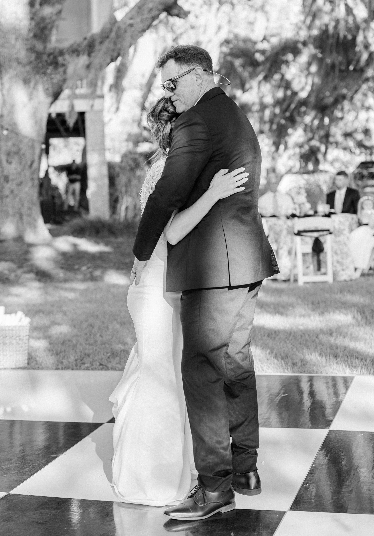 Bride and groom share an emotional first dance embrace on a checkered dance floor at an outdoor wedding reception.
