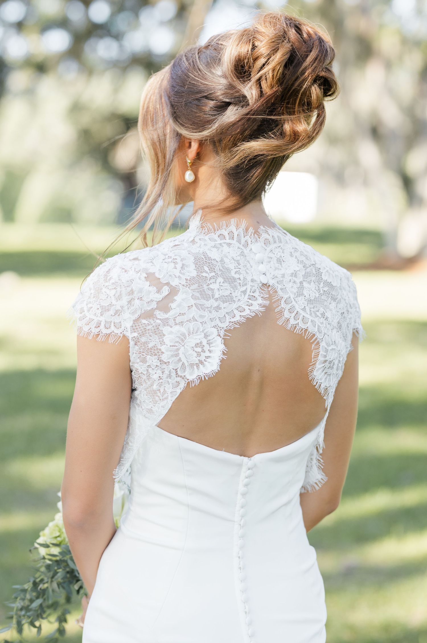 Back view of bride in lace cap sleeve wedding gown with keyhole back and elegant updo hairstyle.
