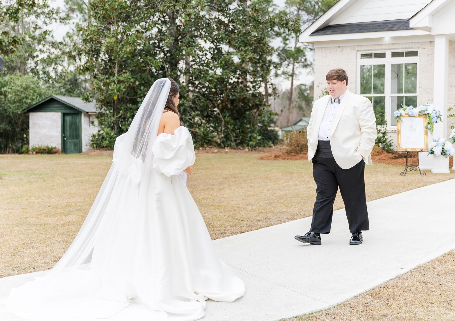Bride in white satin gown and veil shares first look moment with groom in white tuxedo jacket.